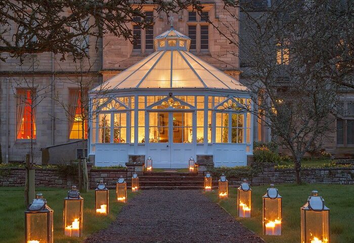 Schloss Roxburghe Hotel's gay-friendly charm. Lantern-lit path leads to a glass conservatory, promising a welcoming escape for gay travelers.