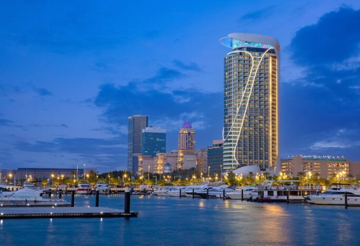 W Dubai - Mina Seyahi, a gay-friendly hotel. View of the hotel at dusk from the water, with boats docked in the foreground.