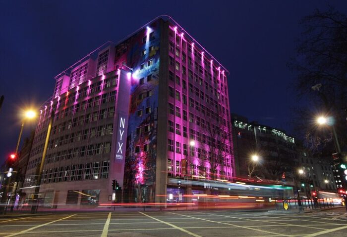 NYX Hotel London Holborn by Leonardo Hotels at night. Gay-friendly hotel with pink lighting and modern design. Urban scene, travel advice.
