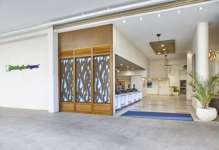 Holiday Inn Express Waikiki lobby. Gay-friendly hotel's modern design with front desk, plants, and the hotel's logo.
