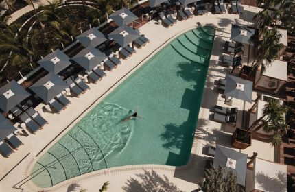 Four Seasons Hotel and Residences Fort Lauderdale pool. Gay-friendly hotel with swimmer, lounge chairs, and umbrellas. Aerial view.
