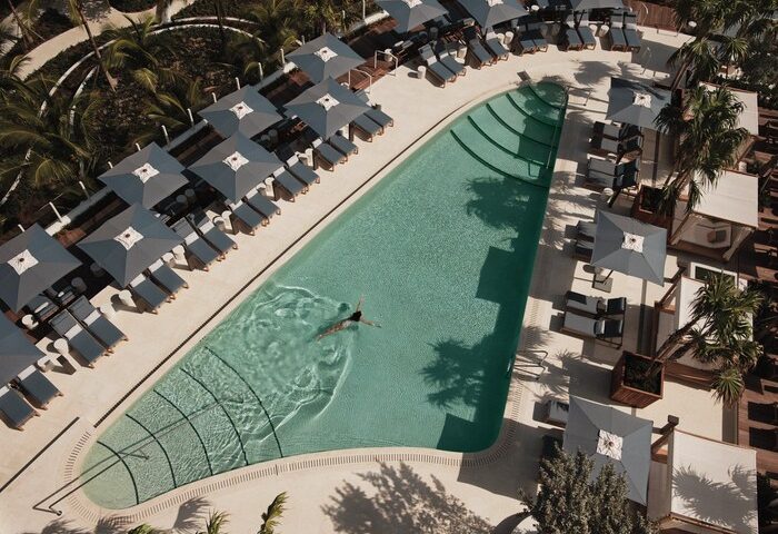 Four Seasons Hotel and Residences Fort Lauderdale pool. Gay-friendly hotel with swimmer, lounge chairs, and umbrellas. Aerial view.