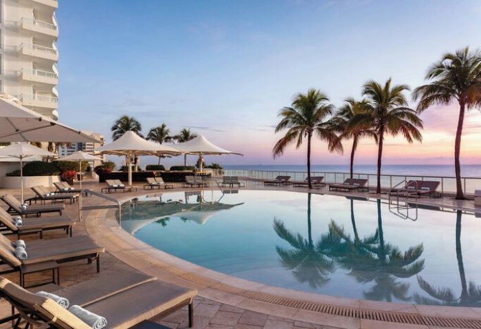 The Ritz-Carlton, Fort Lauderdale gay-friendly hotel pool view. Palm trees, lounge chairs, and ocean at sunset. A luxury travel destination.