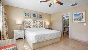 Bedroom at Coconut Bay Resort, a gay-friendly hotel. White bed with patterned headboard, ceiling fan, and bathroom. Comfortable, inviting space.