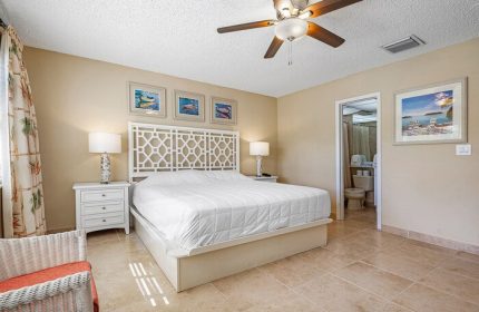 Bedroom at Coconut Bay Resort, a gay-friendly hotel. White bed with patterned headboard, ceiling fan, and bathroom. Comfortable, inviting space.