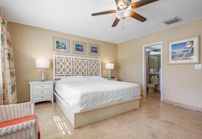 Bedroom at Coconut Bay Resort, a gay-friendly hotel. White bed with patterned headboard, ceiling fan, and bathroom. Comfortable, inviting space.