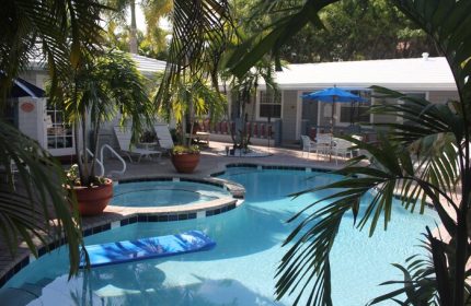 Coral Reef Guesthouse pool view. Gay-friendly hotel with a swimming pool, hot tub, lounge chairs, and tropical plants. Relaxing vacation spot.