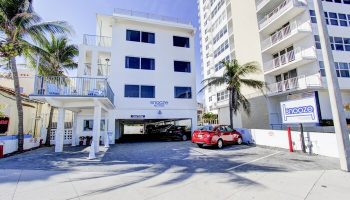 Snooze Hotel, a gay-friendly hotel. White building with parking, palm trees, and a sign. A red car is parked outside. Great for gay travel.