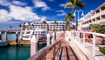Opal Key Resort and Marina's waterfront view. A gay-friendly hotel, marina, and boardwalk with palm trees, boats, and blue skies. Key West travel.