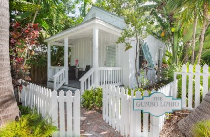 The Paradise Inn adults only gay-friendly hotel: White cottage with porch, picket fence, and The Gumbo Limbo sign surrounded by lush tropical foliage.