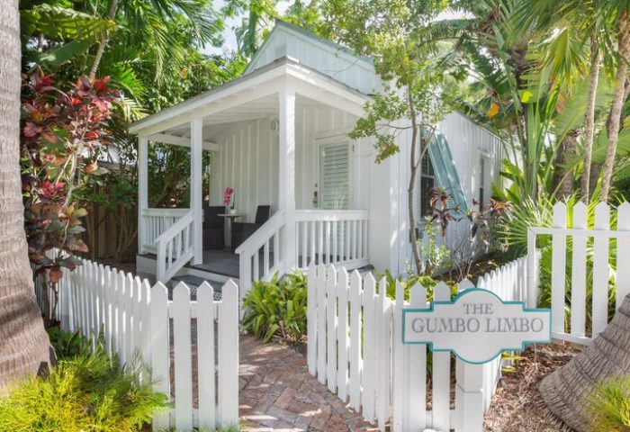 The Paradise Inn adults only gay-friendly hotel: White cottage with porch, picket fence, and The Gumbo Limbo sign surrounded by lush tropical foliage.