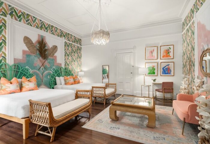 Marrero's Guest Mansion gay-friendly hotel room. Two beds, rattan benches, colorful art, leaf wallpaper, and a peach chair create a stylish space.