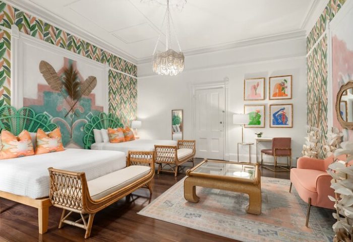 Marrero's Guest Mansion gay-friendly hotel room. Two beds, rattan benches, colorful art, leaf wallpaper, and a peach chair create a stylish space.