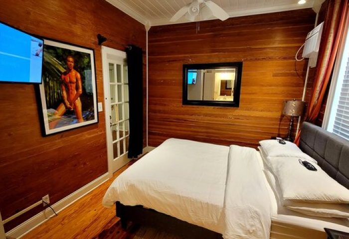 Equator Resort gay-friendly hotel room. Wood paneled walls, white bedding, TV, and art. A comfortable stay for gay travelers.