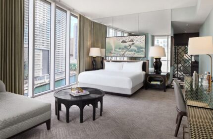 W Miami: Interior of a gay-friendly hotel room. View of the bed, nightstands, and a table. Large windows overlook the city. Modern design.