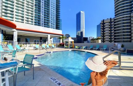 Rooftop pool at Hampton Inn & Suites Miami/Brickell-Downtown, a gay-friendly hotel. Woman in hat relaxes poolside with city skyline view.