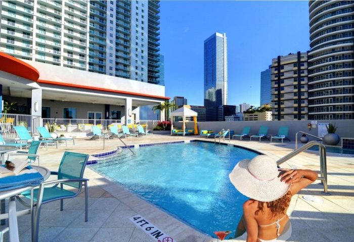 Rooftop pool at Hampton Inn & Suites Miami/Brickell-Downtown, a gay-friendly hotel. Woman in hat relaxes poolside with city skyline view.