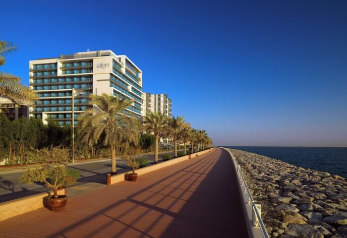 Aloft Palm Jumeirah, a gay-friendly hotel. View of the hotel's exterior from the beachside walking path, with palm trees and blue sky.