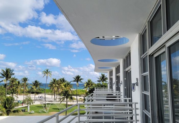 Ocean Drive Suites view from a gay-friendly hotel balcony. Palm trees, beach, and blue sky. A perfect gay travel destination.