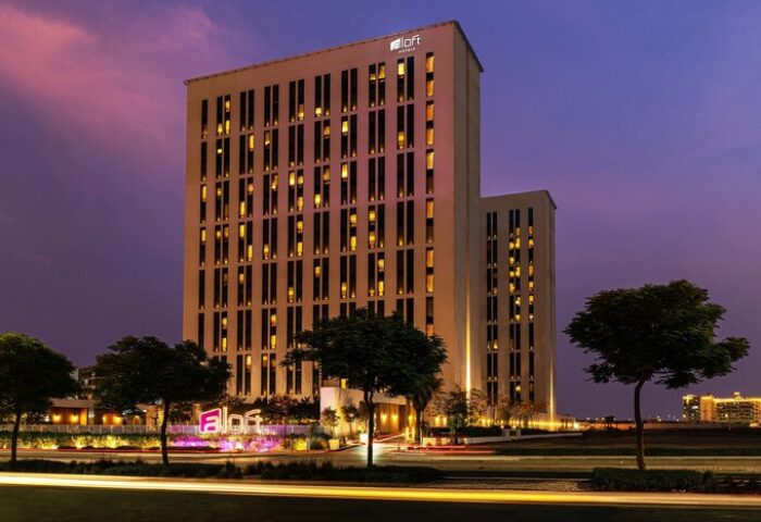 Aloft Me'aisam Dubai, a gay-friendly hotel. Modern architecture with illuminated windows at dusk. A welcoming destination for gay travelers.