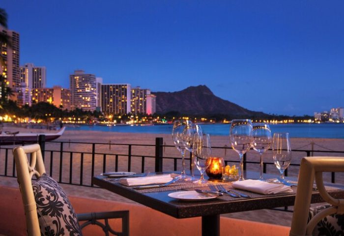 Romantic dinner at The Royal Hawaiian, a Luxury Collection Resort, Waikiki. Gay-friendly hotel with ocean view at dusk. Diamond Head in background.