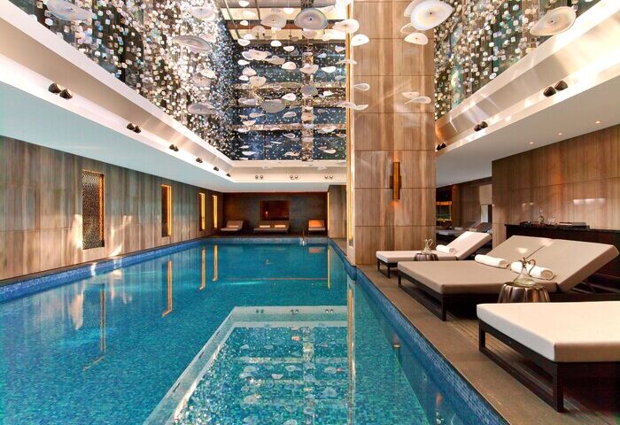 Raffles Istanbul Hotel's indoor pool, a gay-friendly hotel. Elegant design, lounge chairs, and a stunning ceiling installation. Luxury travel.