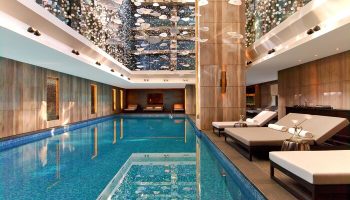Raffles Istanbul Hotel's indoor pool, a gay-friendly hotel. Elegant design, lounge chairs, and a stunning ceiling installation. Luxury travel.