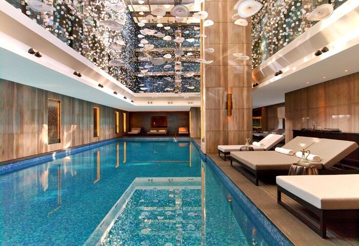 Raffles Istanbul Hotel's indoor pool, a gay-friendly hotel. Elegant design, lounge chairs, and a stunning ceiling installation. Luxury travel.