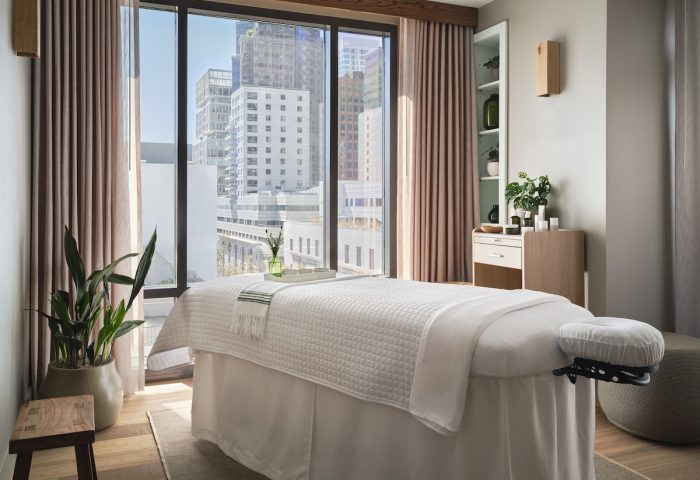 Spa room at 1 Hotel San Francisco, a gay-friendly hotel. Massage table faces a window with a city view. Modern, minimalist design.