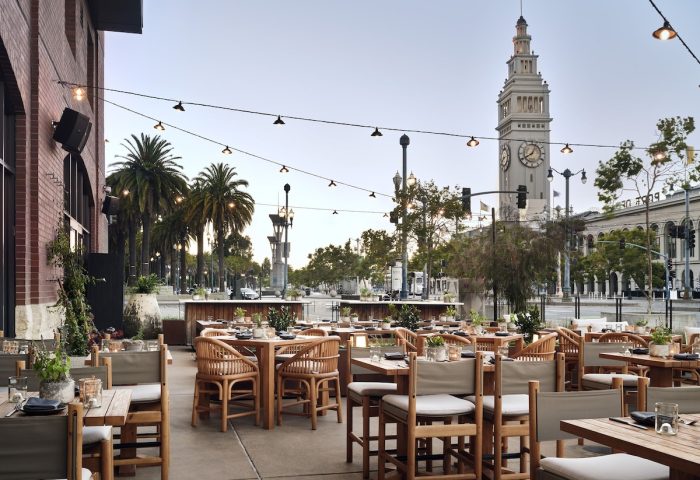 Outdoor dining at 1 Hotel San Francisco, a gay-friendly hotel. Tables set with the Ferry Building in the background. A great hotel for gay men.