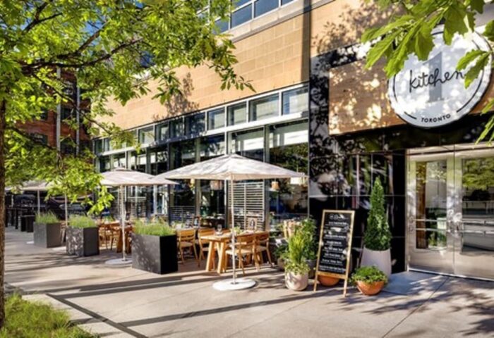 1 Hotel Toronto's Kitchen restaurant. Outdoor dining area with tables, umbrellas, and greenery. A gay-friendly hotel for gay men's travel advice.