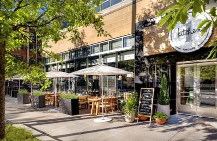 1 Hotel Toronto's Kitchen restaurant. Outdoor dining area with tables, umbrellas, and greenery. A gay-friendly hotel for gay men's travel advice.