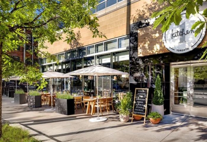 1 Hotel Toronto's Kitchen restaurant. Outdoor dining area with tables, umbrellas, and greenery. A gay-friendly hotel for gay men's travel advice.