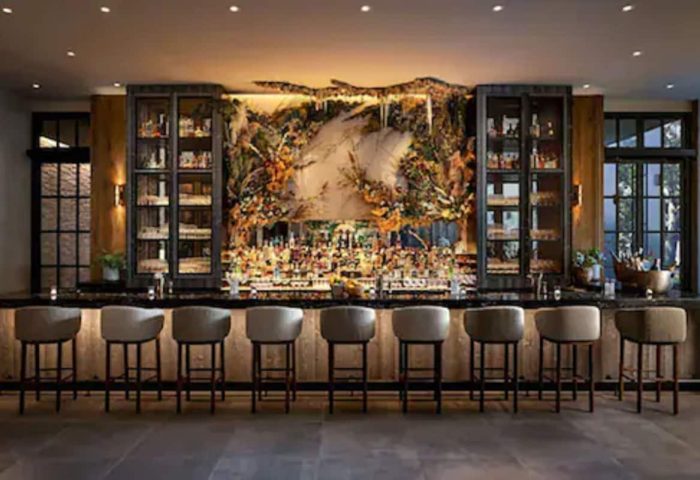 Interior of 1 Hotel Toronto's bar. This gay-friendly hotel bar features a floral backdrop, stools, and liquor cabinets. Upscale and modern.