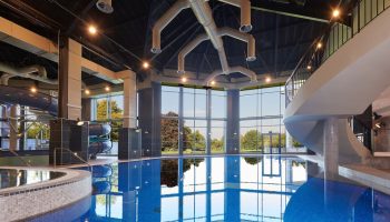 Cameron House on Loch Lomond gay-friendly hotel pool. Blue tiled pool with water slide and floor-to-ceiling windows overlooking greenery.