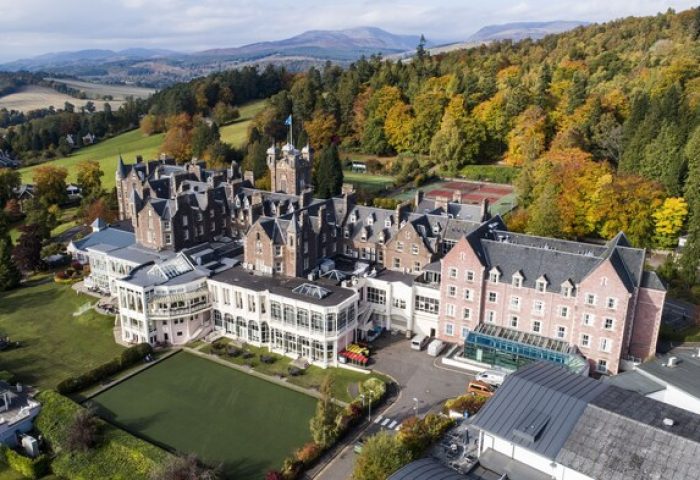 Aerial view of Crieff Hydro, a gay-friendly hotel in Scotland. Resort with mountains, trees, & green lawns. Ideal for gay travel.
