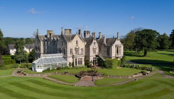 SCHLOSS Roxburghe Hotel, a gay-friendly hotel. Exterior shot of the grand castle hotel with manicured lawns and a bright blue sky. Luxury travel.