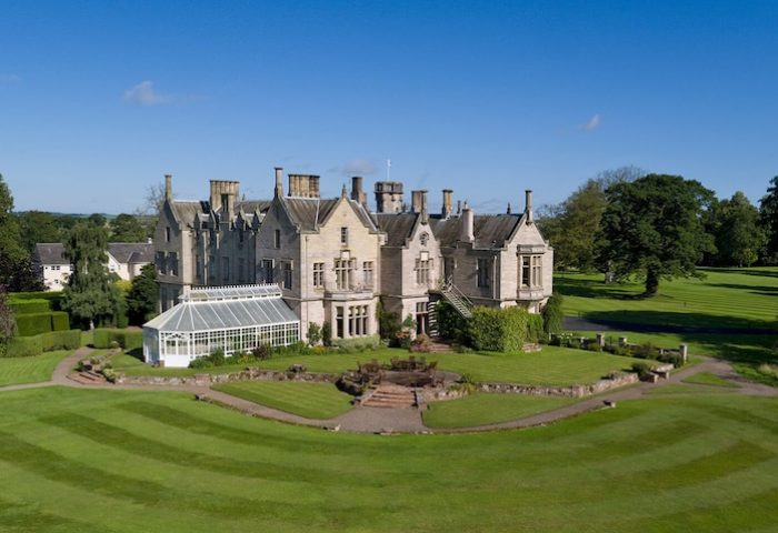 SCHLOSS Roxburghe Hotel, a gay-friendly hotel. Exterior shot of the grand castle hotel with manicured lawns and a bright blue sky. Luxury travel.
