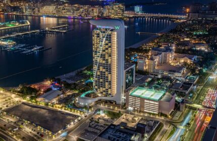 W Dubai - Mina Seyahi gay-friendly hotel at night. Aerial view of the luxury hotel, beach, and city lights. Gay travel advice.