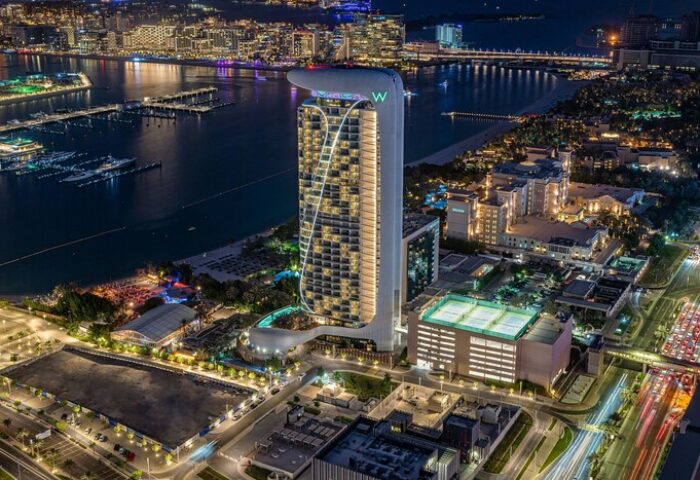 W Dubai - Mina Seyahi gay-friendly hotel at night. Aerial view of the luxury hotel, beach, and city lights. Gay travel advice.