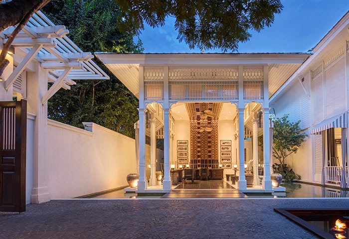 Entrance to 137 Pillars House Chiang Mai, a gay-friendly hotel. White colonial architecture, lush greenery, and tranquil water features.