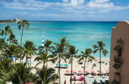 Waikiki beach view from The Royal Hawaiian, a Luxury Collection Resort. Gay-friendly hotel with palm trees, pink umbrellas, and turquoise ocean.
