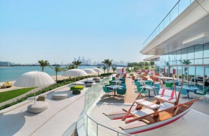 W Dubai - The Palm's beachfront restaurant. Gay-friendly hotel with colorful seating, umbrellas, and a boat-shaped bench overlooking the sea.