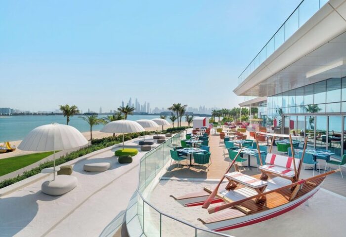 W Dubai - The Palm's beachfront restaurant. Gay-friendly hotel with colorful seating, umbrellas, and a boat-shaped bench overlooking the sea.