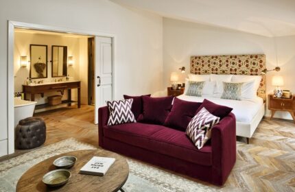 Soho House Istanbul gay-friendly hotel room: Plush burgundy sofa, patterned pillows, king bed, and ensuite bathroom. Luxury gay travel.