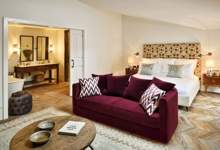 Soho House Istanbul gay-friendly hotel room: Plush burgundy sofa, patterned pillows, king bed, and ensuite bathroom. Luxury gay travel.