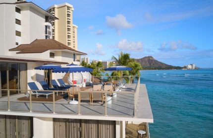 Outrigger Reef Waikiki Beach Resort view. Gay-friendly hotel with oceanfront deck, lounge chairs, umbrellas, and Diamond Head view. Hawaii travel.