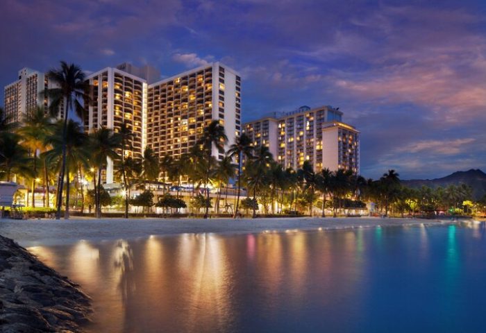 Waikiki Beach Marriott Resort & Spa at dusk. Gay-friendly hotel on the beach with palm trees. Diamond Head in the background. Night scene.
