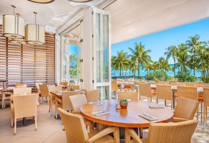 Hyatt Regency Waikiki Beach Resort's open-air restaurant. Tables with wicker chairs overlook palm trees and the ocean. Gay-friendly hotel dining.