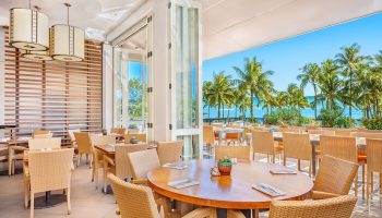Hyatt Regency Waikiki Beach Resort's open-air restaurant. Tables with wicker chairs overlook palm trees and the ocean. Gay-friendly hotel dining.
